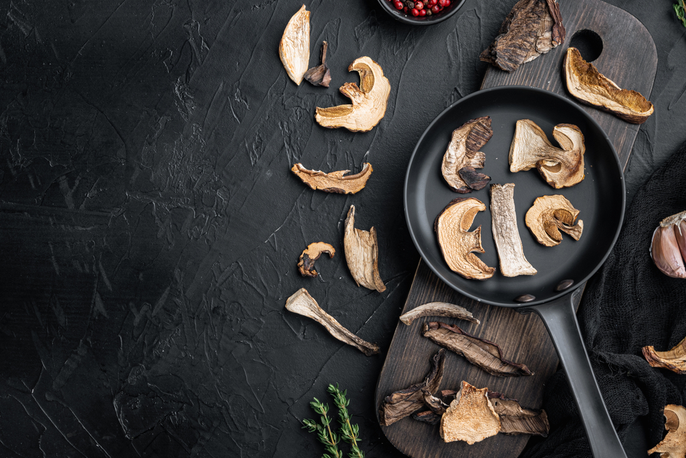 Wild organic dried porcini mushroom in cast iron skillet, on black background, top view flat lay, with room for text copyspace
