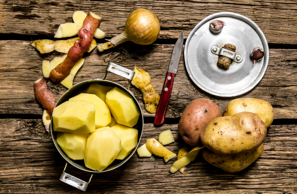 Eating potato.  Peeled potatoes in an old pan with knife on wooden table.  top view